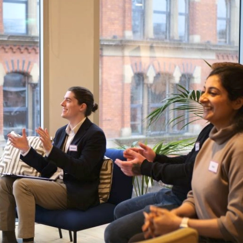 Audience of professionals clapping and smiling while watching a participant practise public speaking during Project Charisma’s 1-Day Masterclass in Manchester
