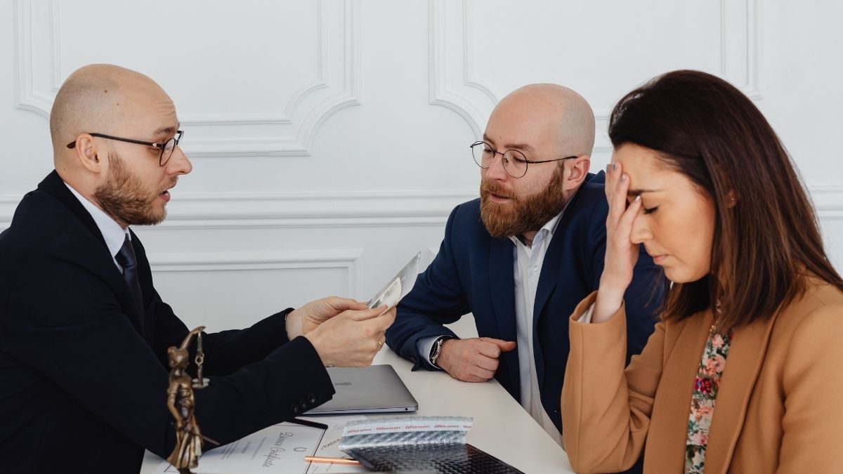 Three professionals in a heated discussion, with one woman looking frustrated and holding her head