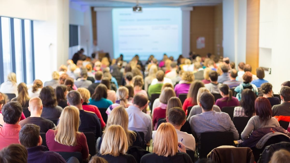 Large audience seated in a conference hall watching a keynote speaker on stage