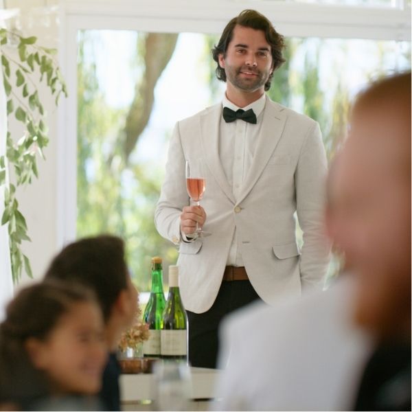 Best man dressed in white standing up to begin his best man speech at a wedding reception