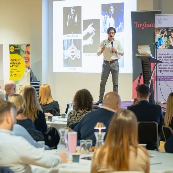 Ed Darling delivering his keynote talk "Speaking with Impact" on stage at a large professional conference in Belfast
