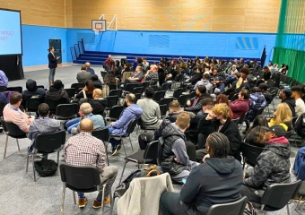 Ed Darling delivering a talk on confidence and communication skills to a large group of students and staff at UCEN Manchester in a sports hall
