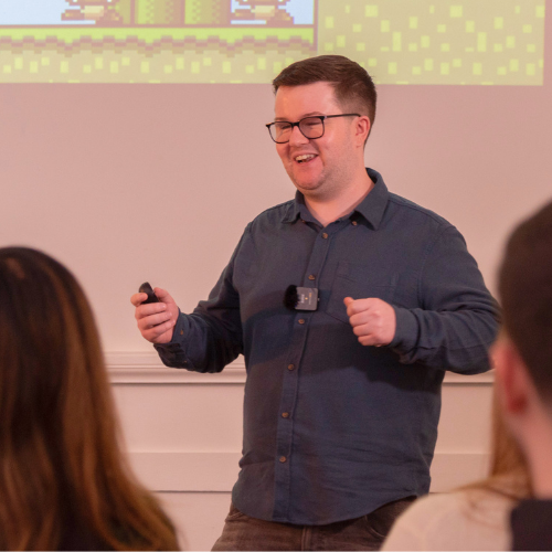 Man practising advanced communication skills while being recorded during a Project Charisma public speaking workshop, learning alongside a group of peers