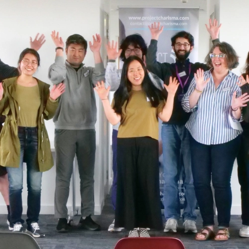 PHD students and faculty at University of Manchester Alliance Business School smiling with hands up after completing Project Charisma public speaking training course